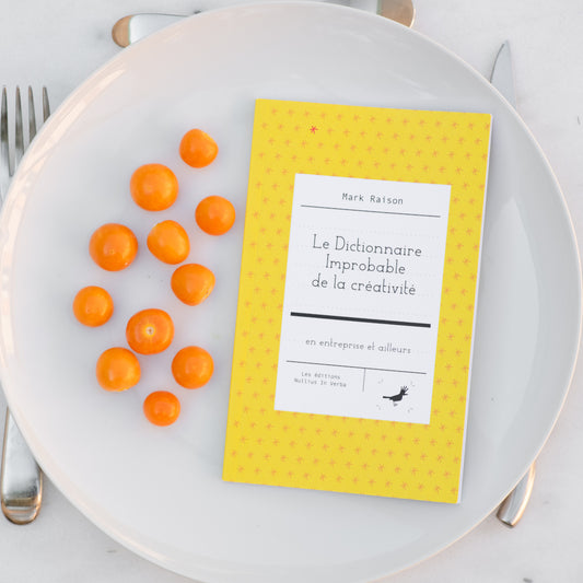 Le livre est disposé dans une assiette avec des cerises de terre. On voit une fourchette, un couteau et une cuiller autour de l'assiette.