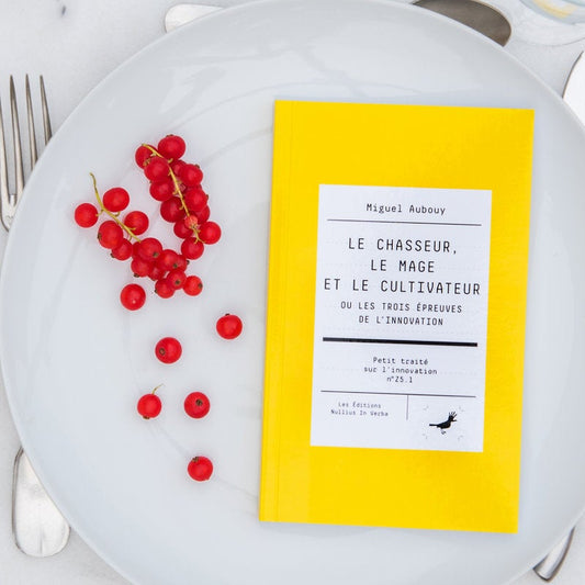 Le livre est disposé dans une assiette avec des groseilles. On voit une fourchette, un couteau et une cuiller autour de l'assiette.