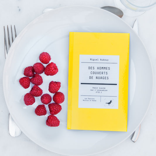Le livre est disposé dans une assiette avec des framboises. On voit une fourchette, un couteau et une cuiller autour de l'assiette.