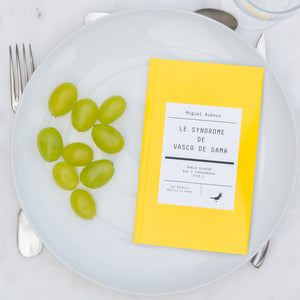 Le livre est disposé dans une assiette avec des raisins italiens. On voit une fourchette, un couteau et une cuiller autour de l'assiette.