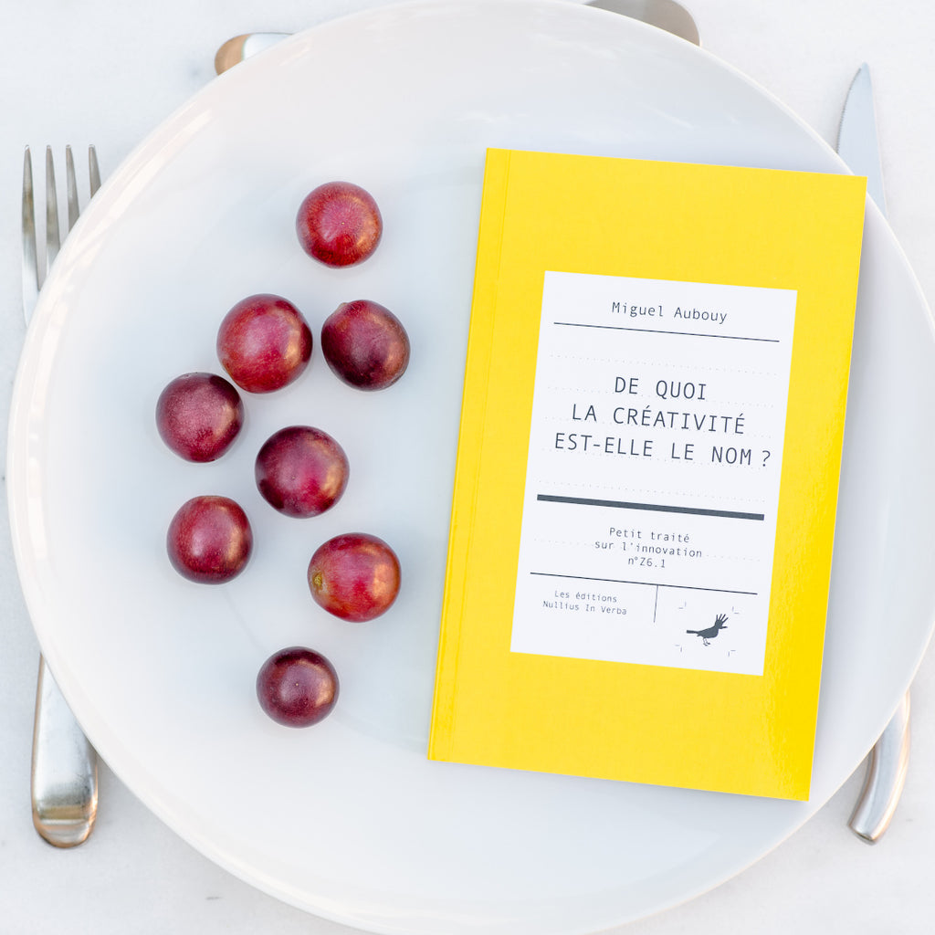 Le livre est disposé dans une assiette avec des grains de raisins. On voit une fourchette, un couteau et une cuiller autour de l'assiette.